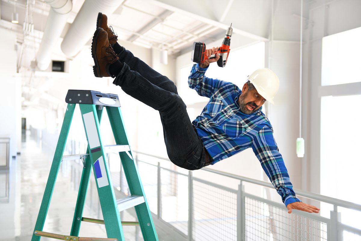 A worker falling backward off a ladder while holding a power drill