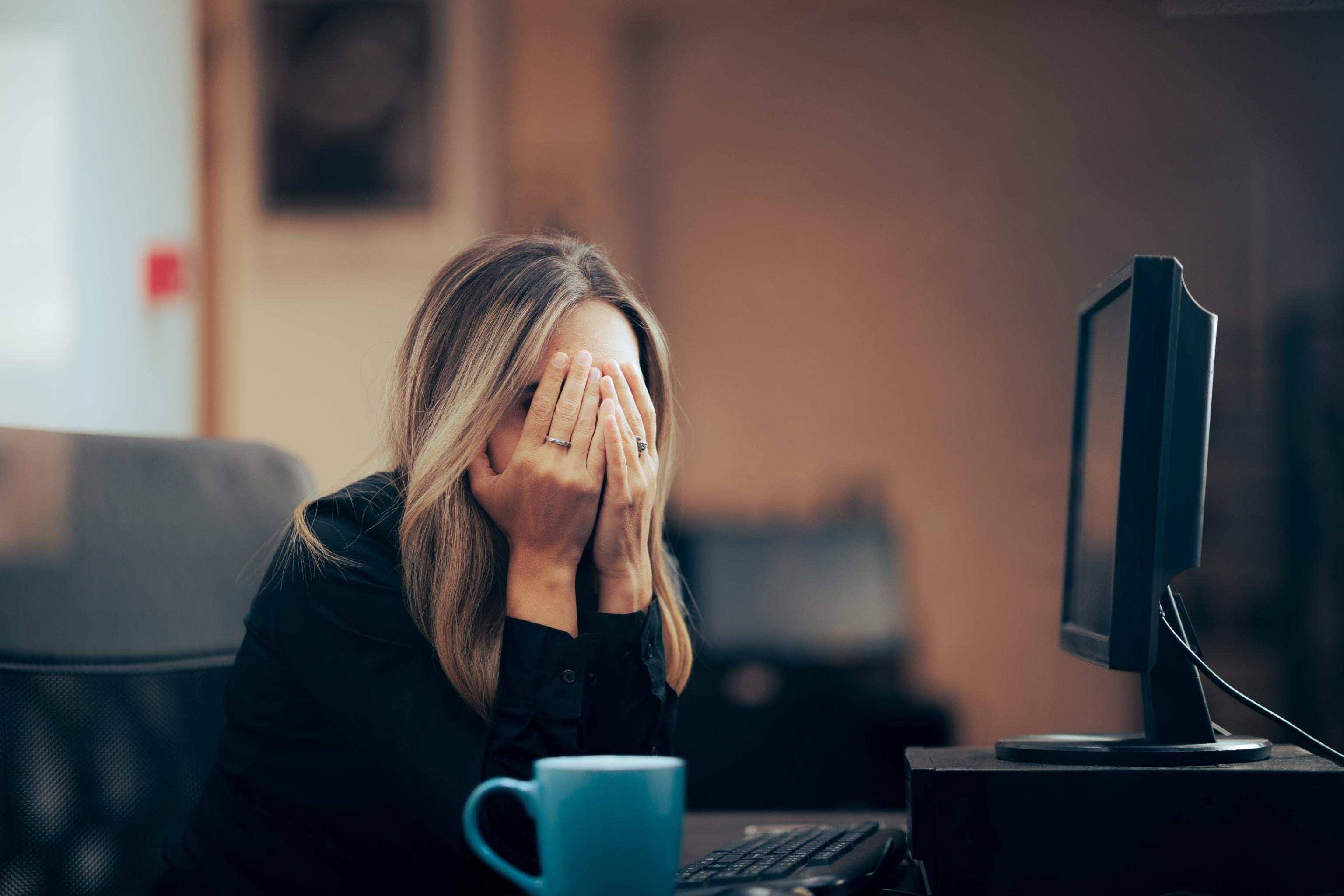 A distressed woman covering her face while sitting at her desk at work